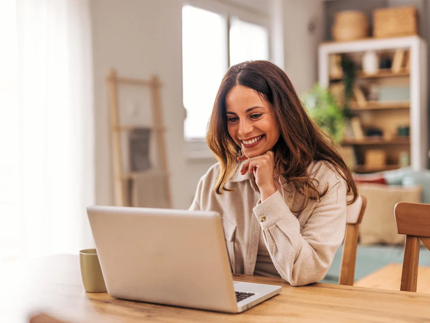 Smiling woman with her hand on her chin, using her laptop in her stylish living room.